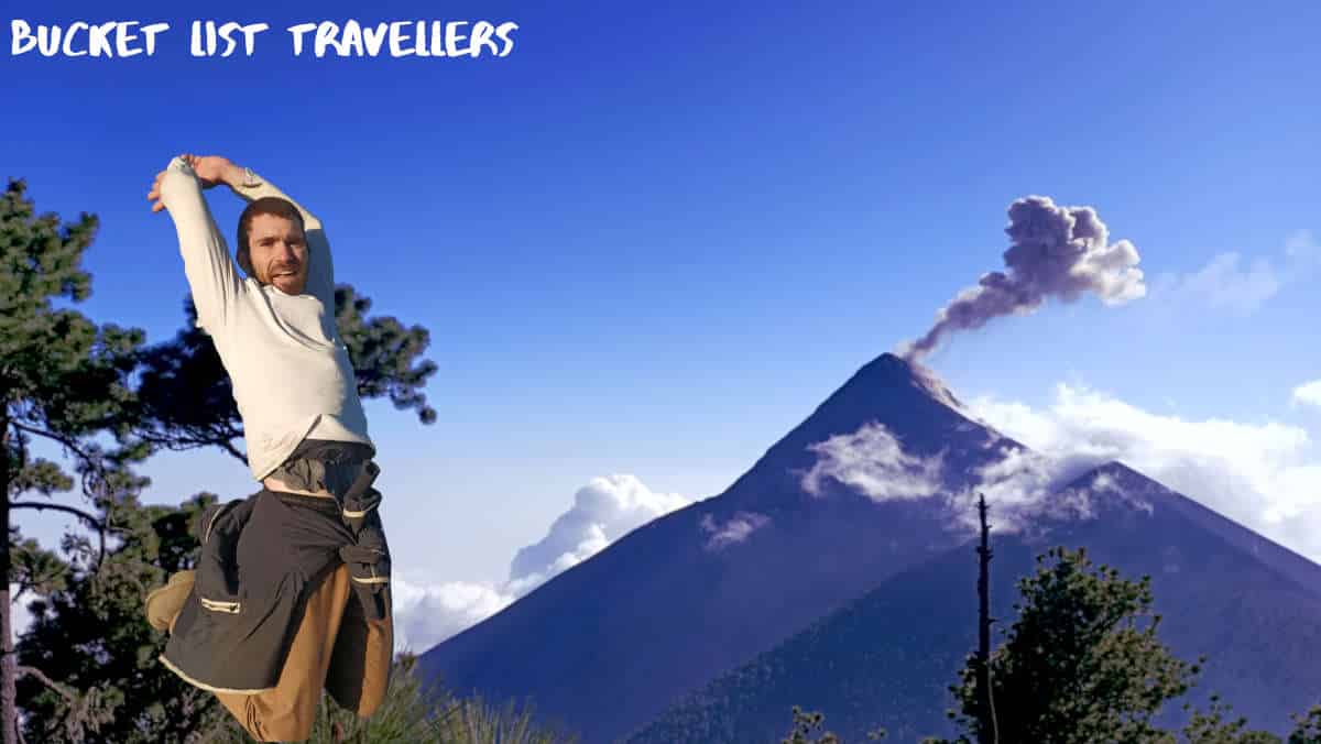 Smoke rising from Fuego Volcano Guatemala, man jumping in front of erupting volcano, man in white shirt and brown pants