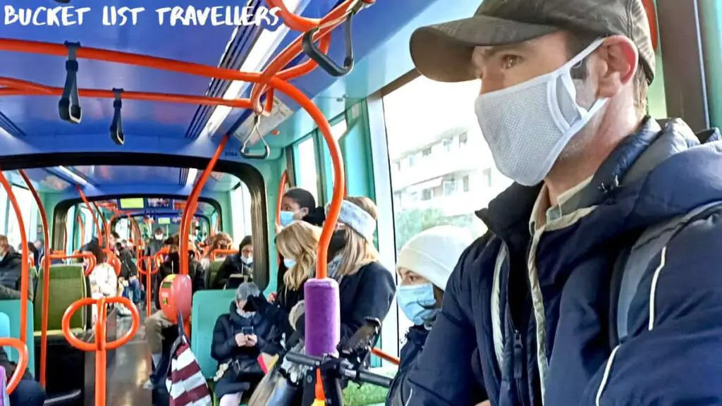 Man sitting on Tram in Montpellier France, passengers wearing masks, blue ceiling, red handrails