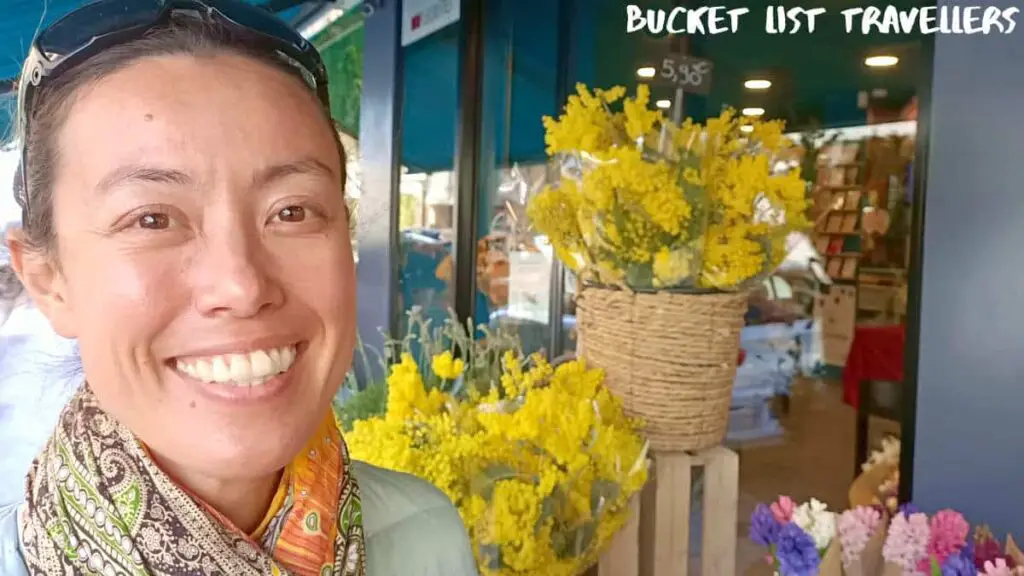 Woman smiling outside a florist in Nice France, bouquets of golden wattle and other flowers