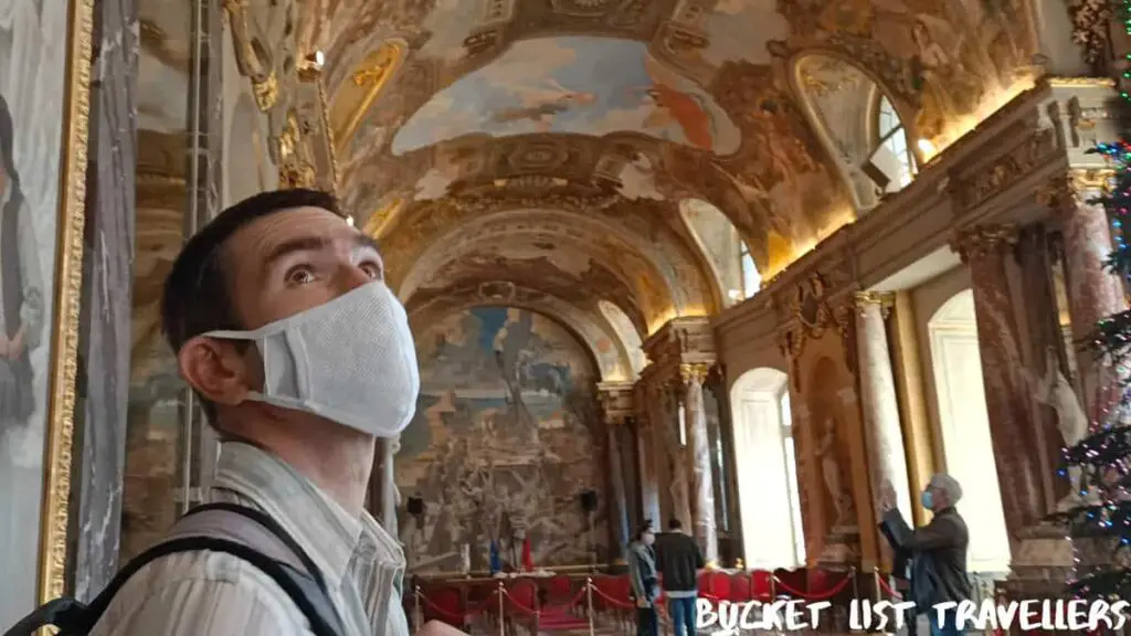 Man wearing white mask looking up at painted ceiling in Le Capitole Toulouse France