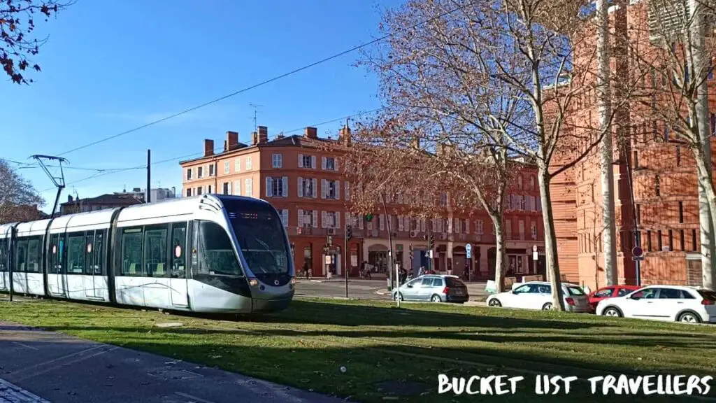 Tram on Esplanade des Français d'Afrique du Nord Toulouse France, green grass, blue sky, pink buildings