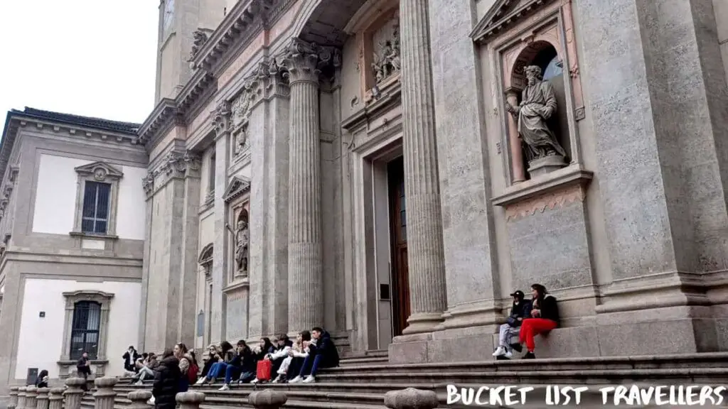 People sitting on stairs outside Chiesa di Sant'Alessandro in Zebedia Milan Italy