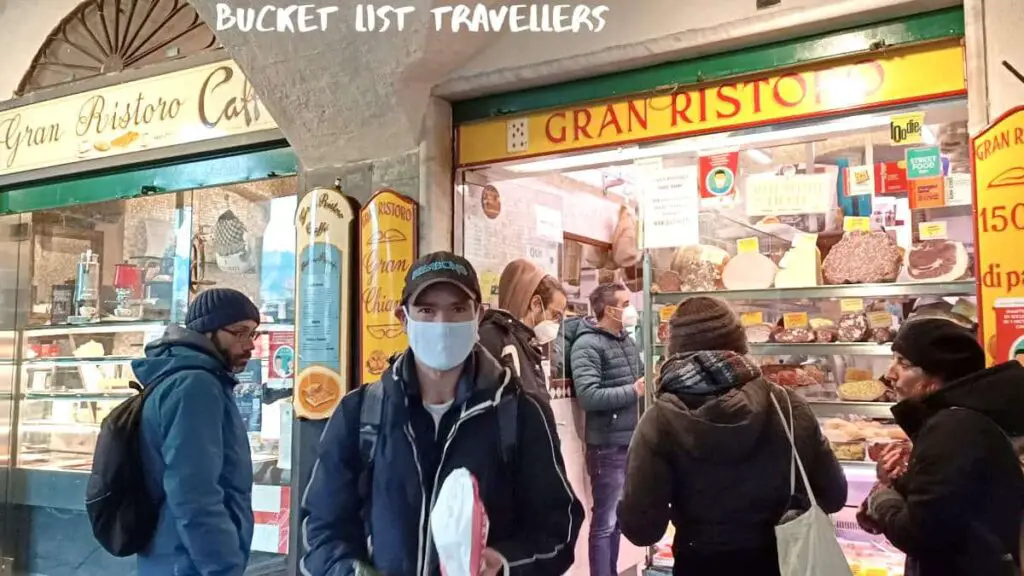 Customers waiting outside Gran Ristoro Genoa Italy, man wearing white mask holding paper bag