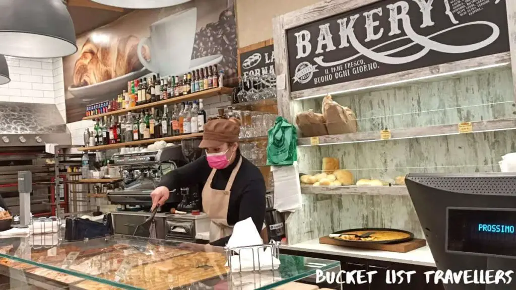 La Fornarina Bakery Sanremo Italy, staff wearing pink mask and reaching for slice of pizza