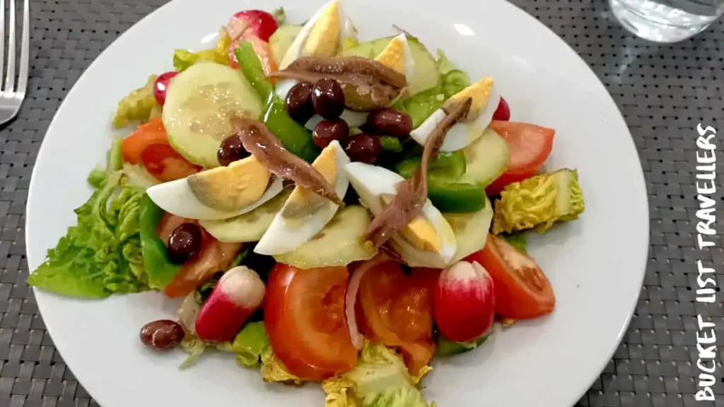 Niçoise Salad Nice France, eggs, anchovies, olives, tomatoes, radishes, lettuce, green bell pepper, cucumber, white plate