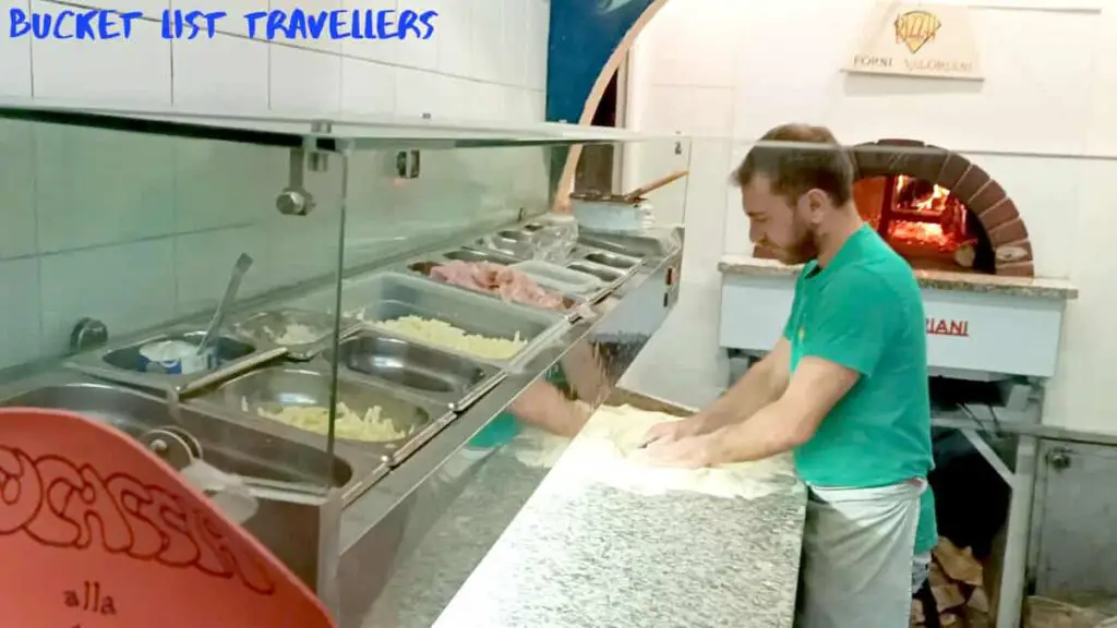 Man kneeding dough to make pizza at Pizza Power Sanremo Italy, wood fire oven in background