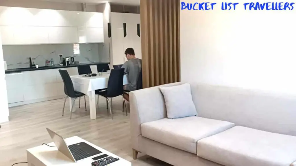 Accommodation Tirana Albania, lounge room, kitchen and dining room in modern apartment in Albania, man sitting at dining room table on laptop