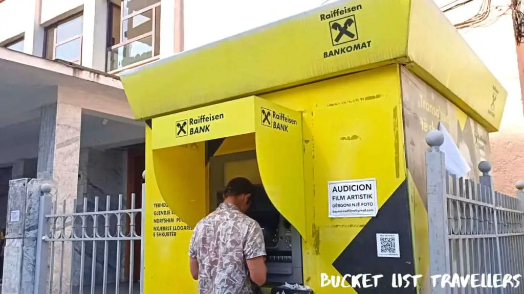 Man at ATM in Shkodra Albania, Raiffeisen Bankomat ATM, yellow ATM booth