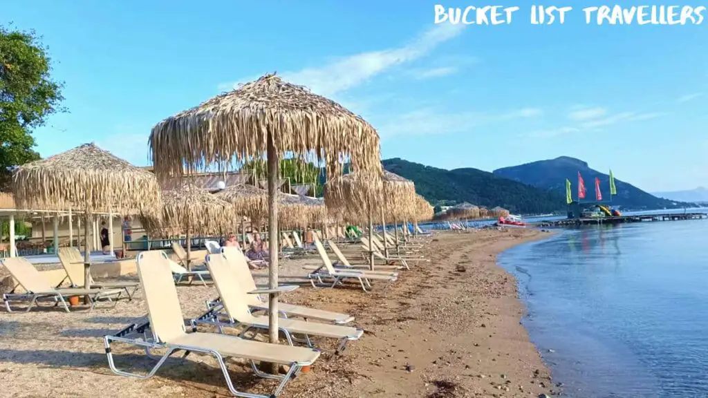 Beach loungers at Moraitika Beach Corfu Greece, straw umbrellas, sandy beach, mountains in background