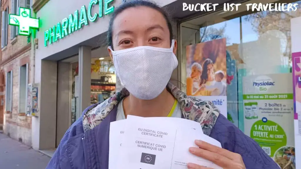 Woman starting outside pharmacy in France holding EU Digital Covid Vaccination Certificate