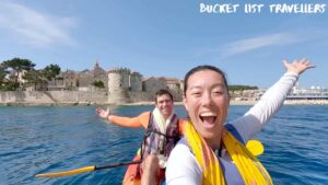 Woman and Man smiling with arms in air on kayak in front of Korcula Old Town, Couple Kayaking at Korcula Old Town Croatia