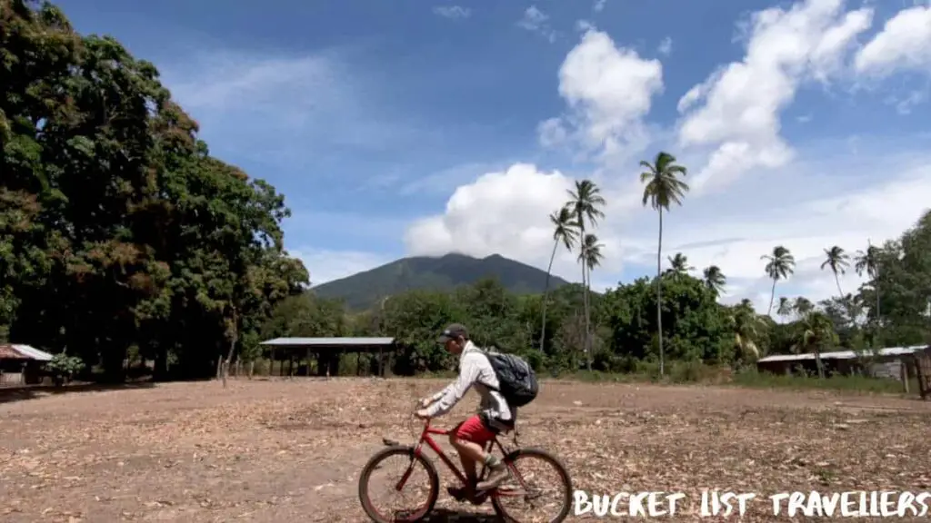 Cycling Merida Ometepe Island Nicaragua, man cycling with Volcan Madera and palm trees in the distance